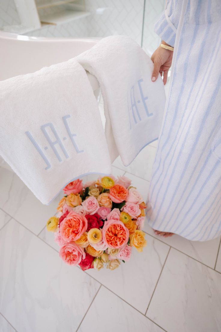 a person holding two towels with flowers on them in front of a bath room sink