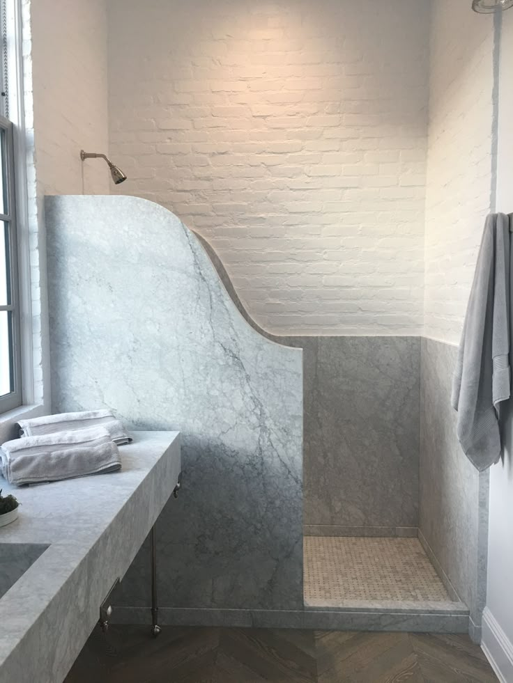 a bathroom with white walls and marble counter tops, along with a large window that looks out onto the outside