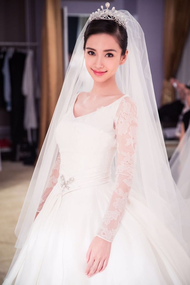 a woman in a wedding dress and veil posing for the camera with her hands on her hips