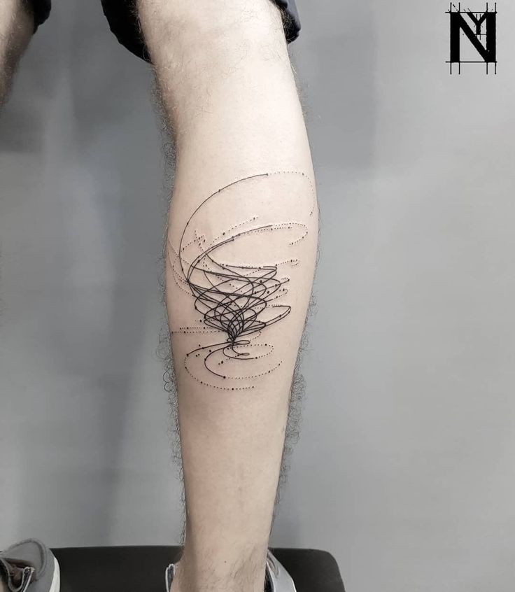 a man's leg with lines and circles tattoo on his right calf area, while he is sitting on a black suitcase