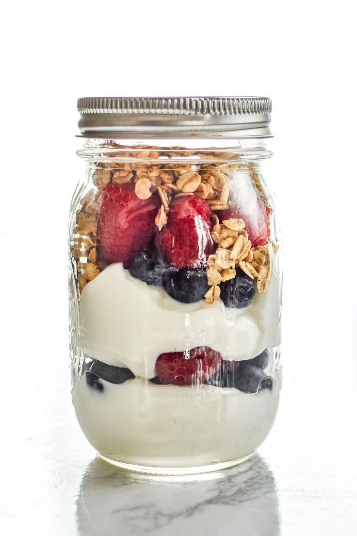 a glass jar filled with yogurt, granola and strawberries on top