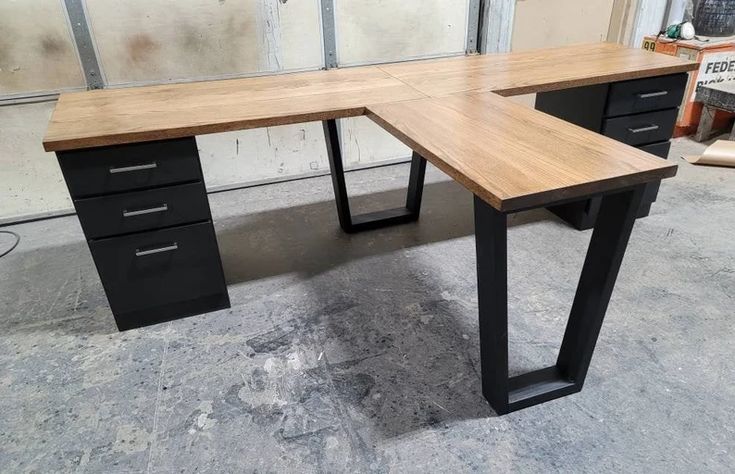 a wooden desk with two black drawers and one light wood top, in a garage