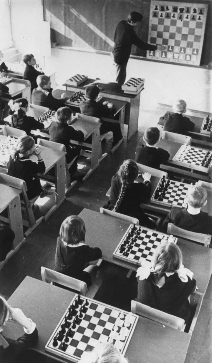 an old black and white photo of children playing chess in school uniforms with their teacher