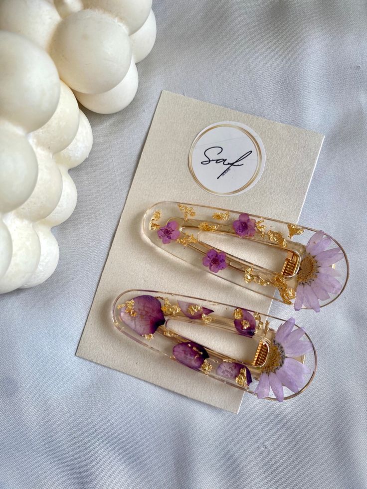 two pieces of jewelry sitting on top of a table next to some white rocks and flowers