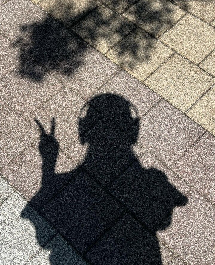 a shadow of a person holding a cell phone in their hand and standing on the sidewalk