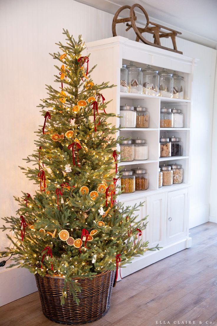 a small christmas tree in a basket next to a shelf with jars and spices on it