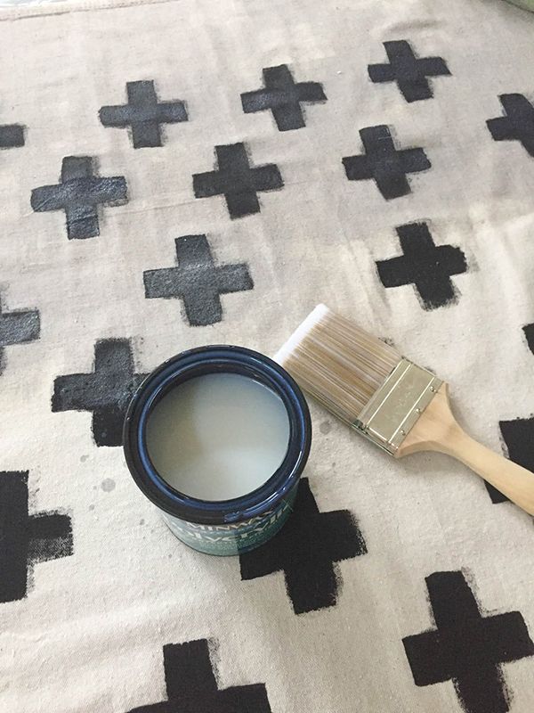 a paint can and brush sitting on top of a white rug covered in black crosses