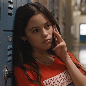 a woman leaning against a locker while talking on a cell phone and looking at the camera