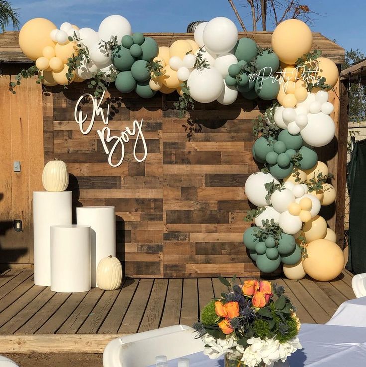 an outdoor wedding setup with balloons and greenery on the wall, along with flowers