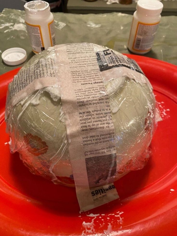 a paper mache sitting on top of a red plate covered in plastic wrapper