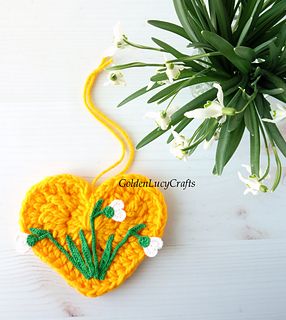 a crocheted heart with flowers on it next to a small potted plant