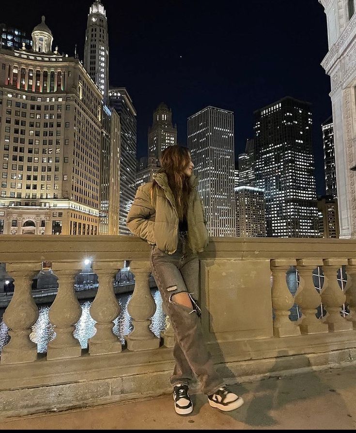 a woman sitting on top of a stone wall next to a city skyline at night