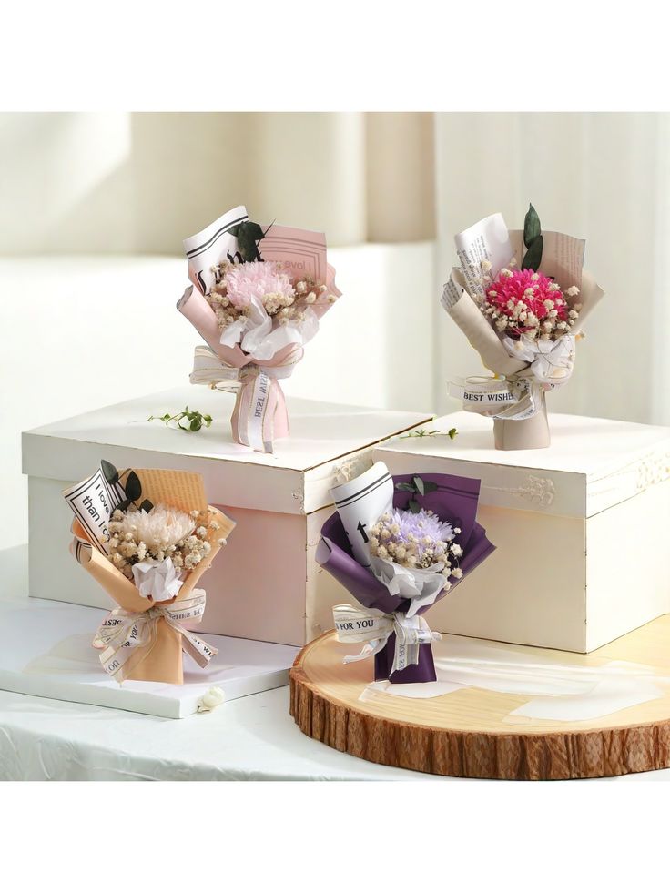 three small bouquets of flowers are sitting on top of each other in white boxes