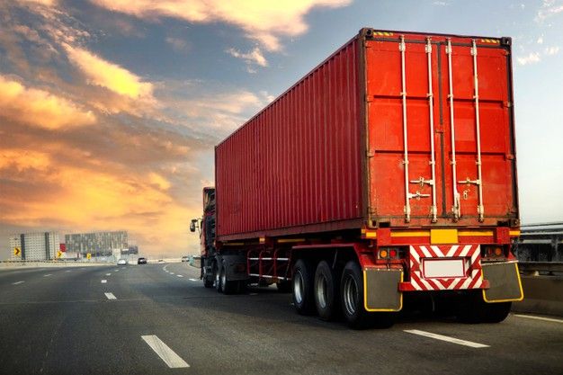 a large red truck driving down a highway under a cloudy blue and yellow sky with clouds