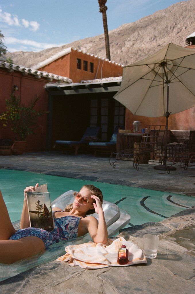 a woman laying on the ground next to a pool with an open book in her hand