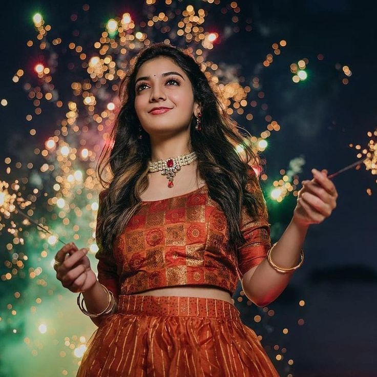 a woman in an orange lehenga holding a sparkler and looking up at the sky