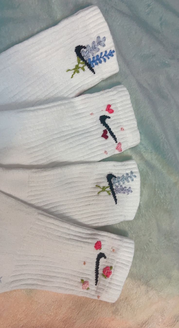 three pairs of socks with embroidered flowers on them sitting next to the ocean and sand