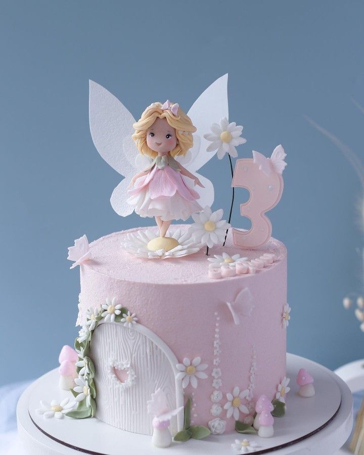 there is a pink cake with a fairy on top and daisies around the edge