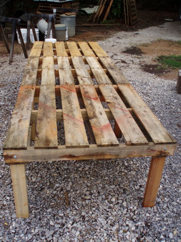 a table made out of wooden pallets on gravel with chairs in the back ground