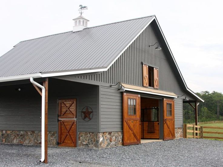 a large gray barn with two doors and a porch on the side of it, in front of a green field