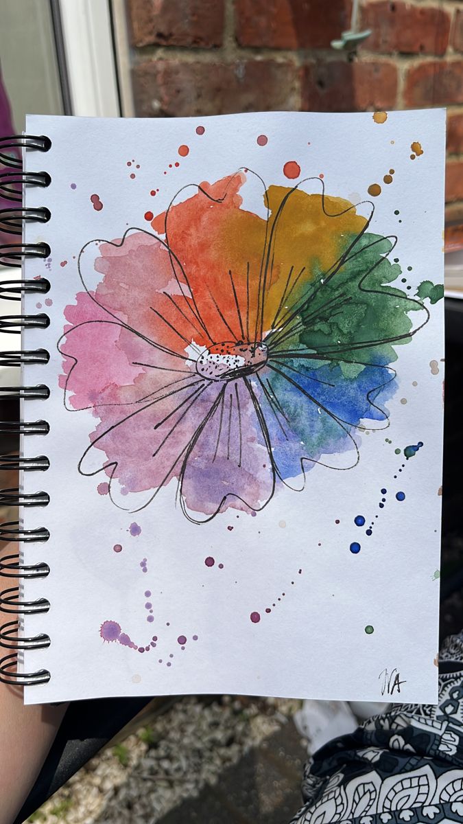 a person holding up a piece of paper with watercolor paint on it and a drawing of a flower in the middle