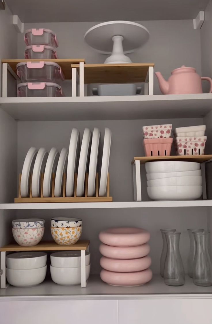 the shelves are filled with dishes, cups and other kitchen wares in pink and white