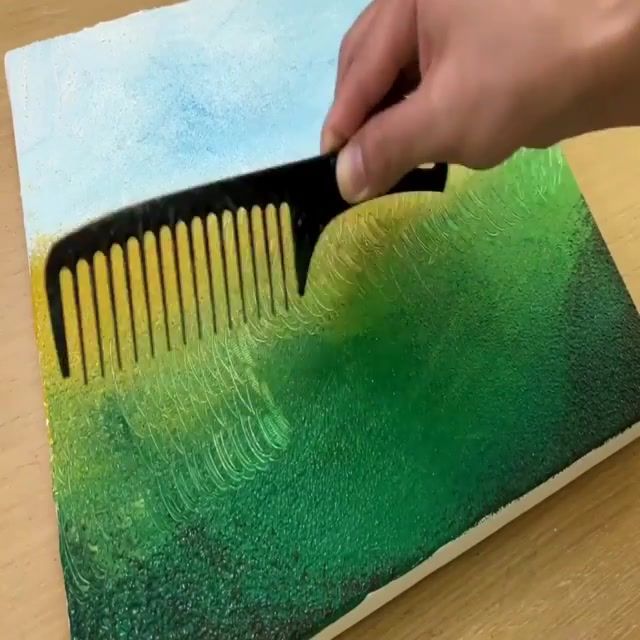 a person is using a comb to brush the green and yellow paint on a piece of paper