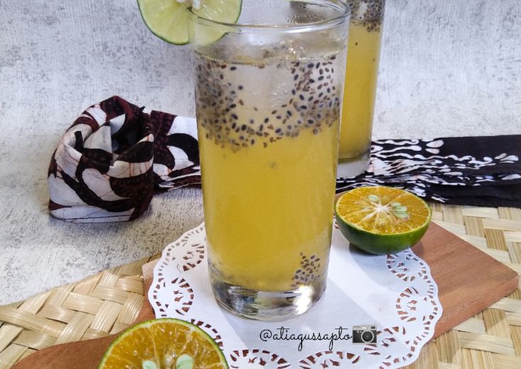 two glasses filled with liquid sitting on top of a wooden tray next to sliced oranges