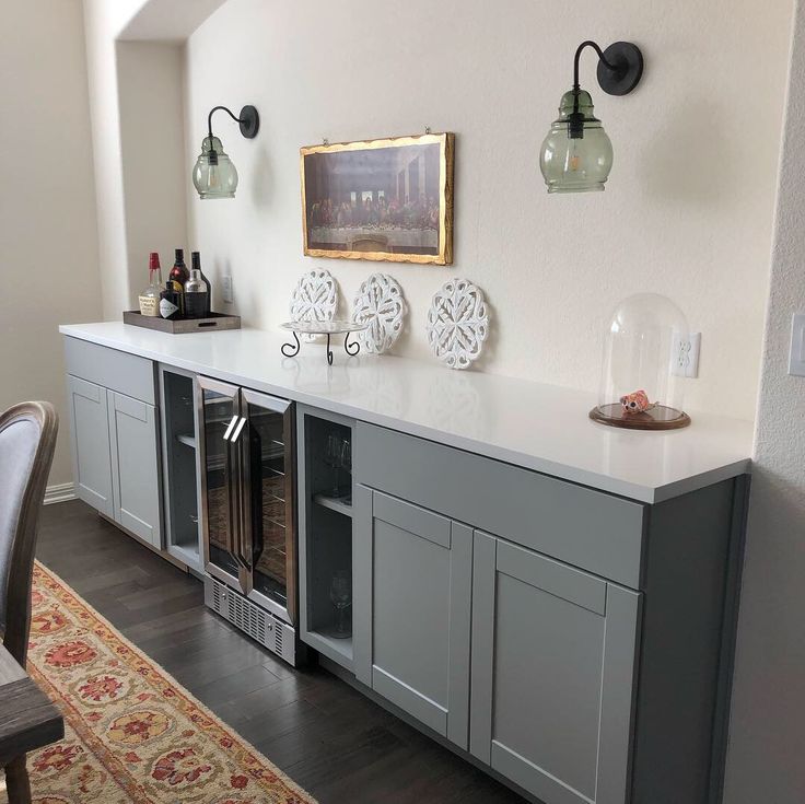 a kitchen area with gray cabinets and white counter tops, two wine glasses on top of the cabinet doors