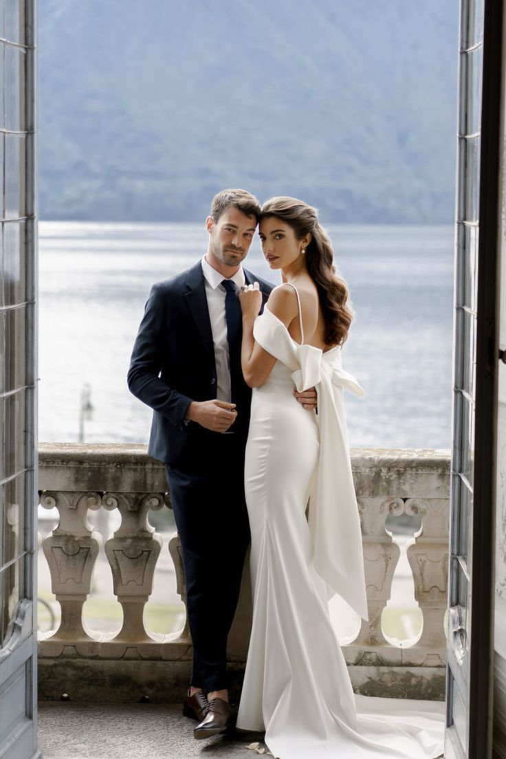 a man and woman standing next to each other in front of an open door with the water behind them