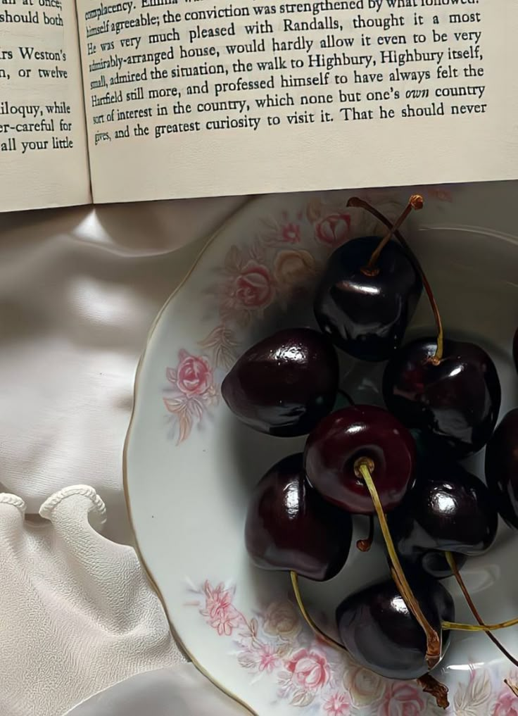 a bowl filled with cherries next to an open book