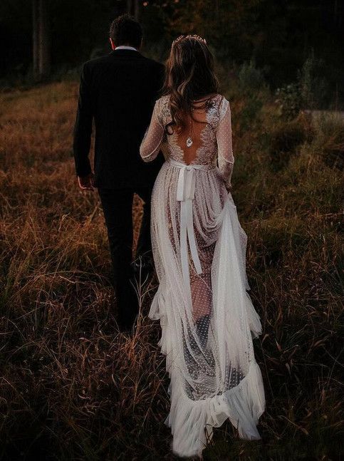 a man and woman are walking through the grass together, dressed in wedding dresses with sheer fabric