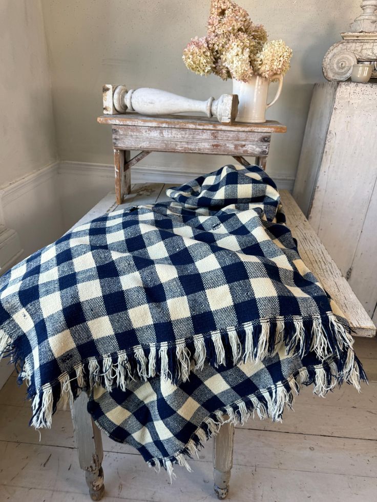 a blue and white checkered blanket sitting on top of a wooden bench next to a vase with flowers