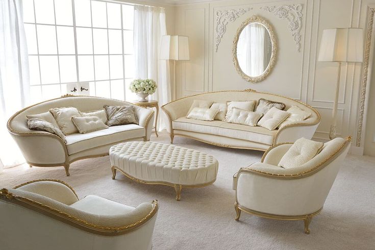 a living room filled with white furniture next to a large window and a mirror on the wall