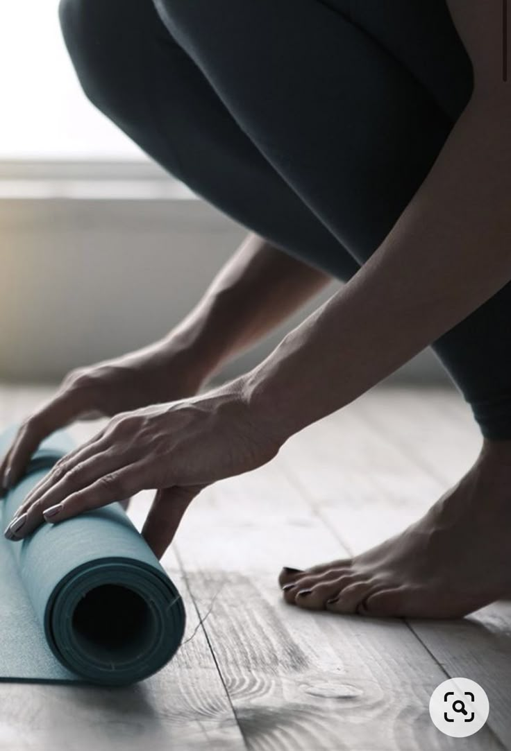 a woman rolling up a blue yoga mat on the floor with her hands and feet