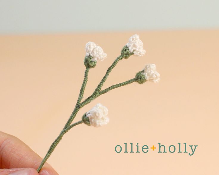 a hand holding a tiny crocheted white flower