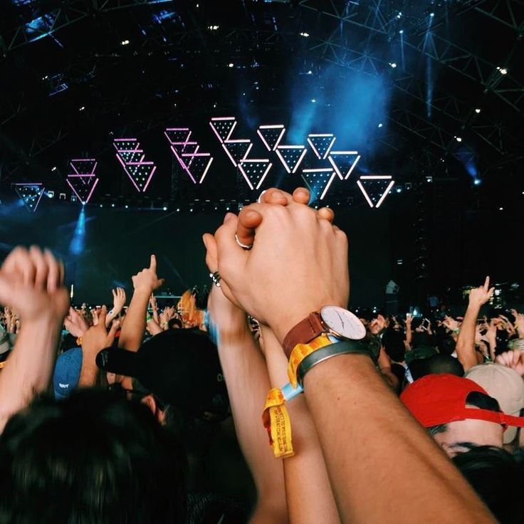 many people are at a concert with their hands in the air and lights above them