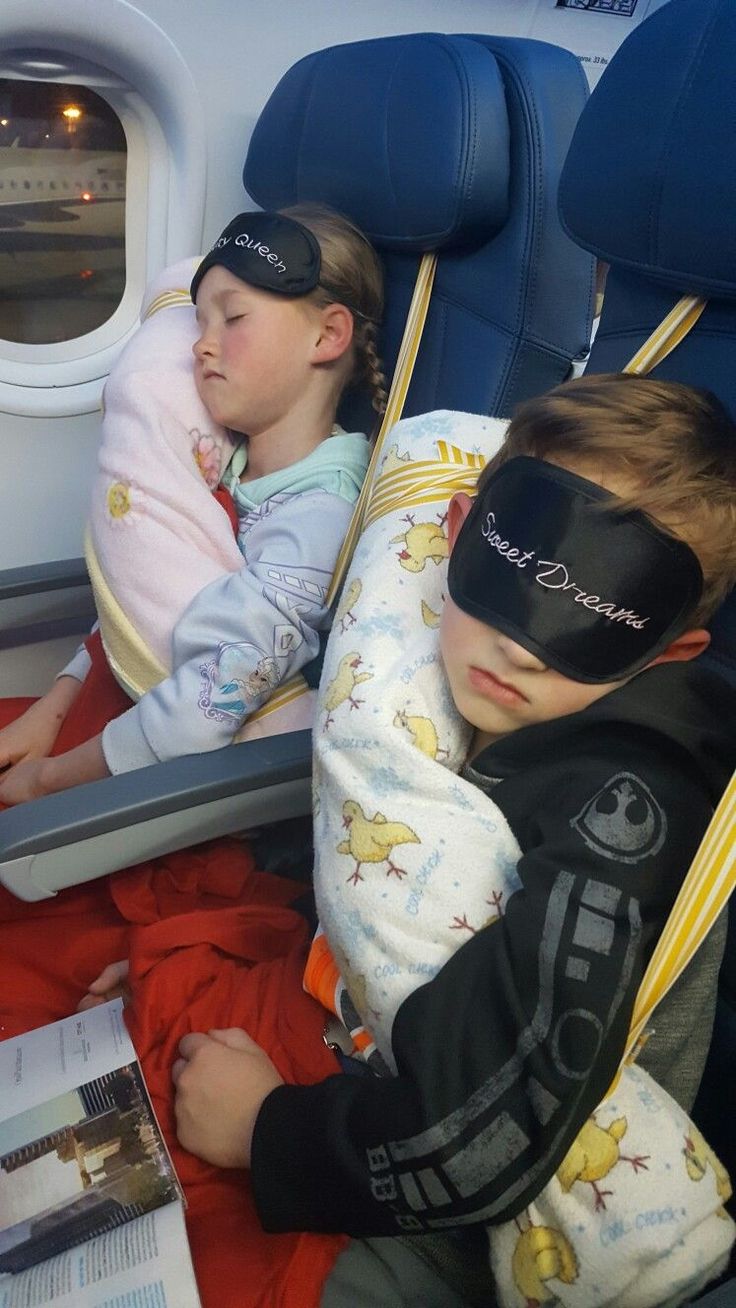 two children sleeping on an airplane seat with blindfolds over their eyes as they look out the window