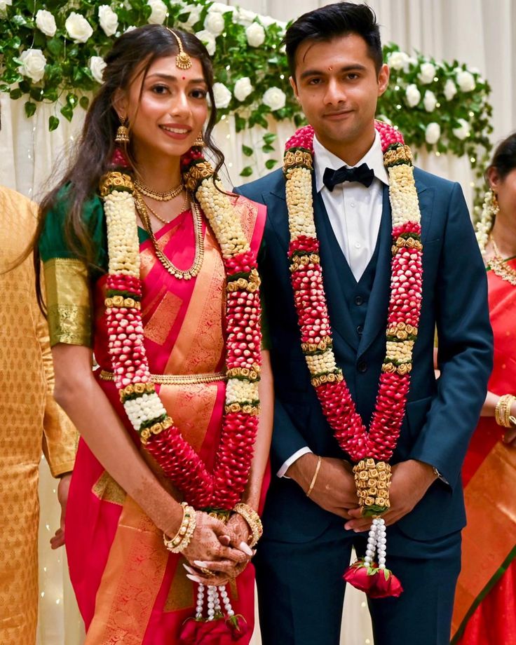 two people standing next to each other wearing red and gold sari with flowers on them