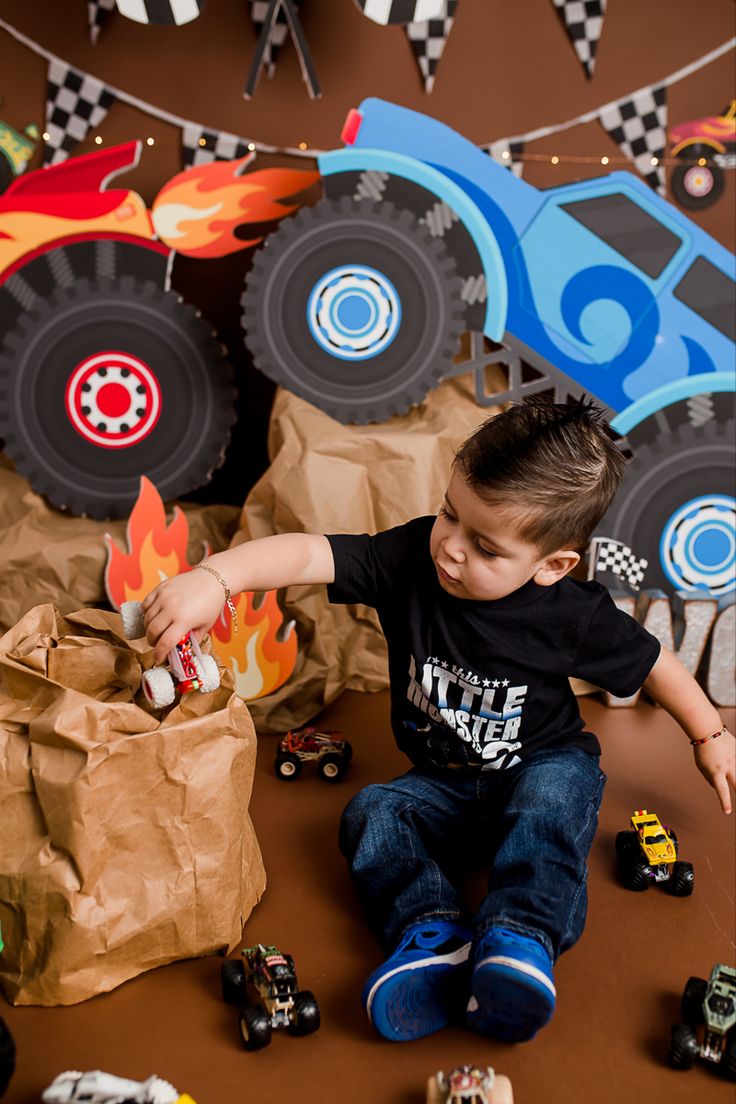 a young boy sitting on the floor next to toy cars and paper bags filled with toys