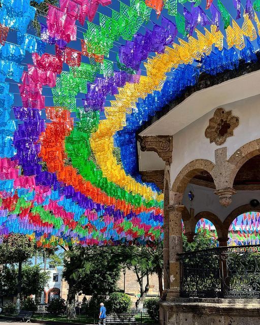 colorful paper streamers hanging from the ceiling in front of a building with people walking by