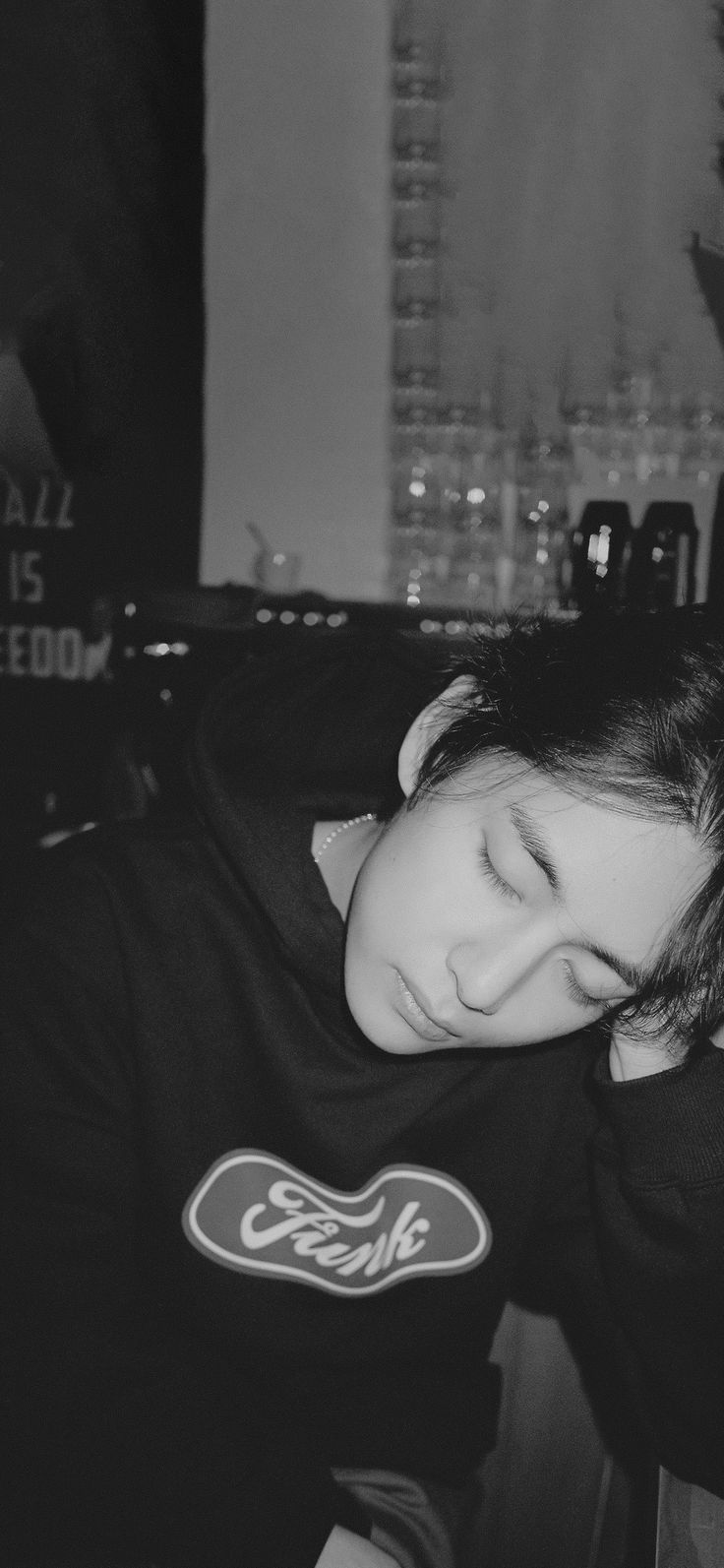 black and white photograph of a young woman sleeping in front of a computer desk with her head on her hands