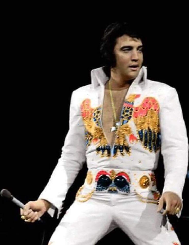 elvis presley performing on stage in white suit with gold and red decorations, holding a microphone