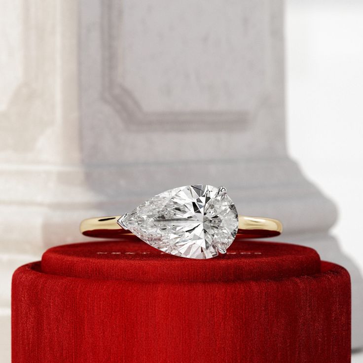 a heart shaped diamond ring sitting on top of a red velvet box in front of a pillar