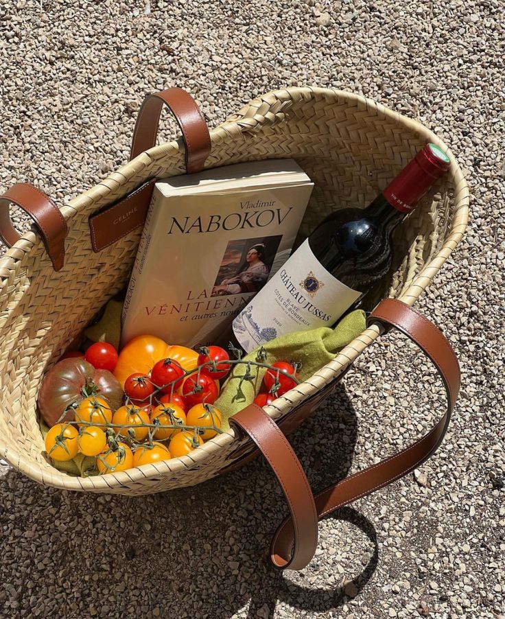 a basket filled with assorted fruits and vegetables next to a bottle of red wine