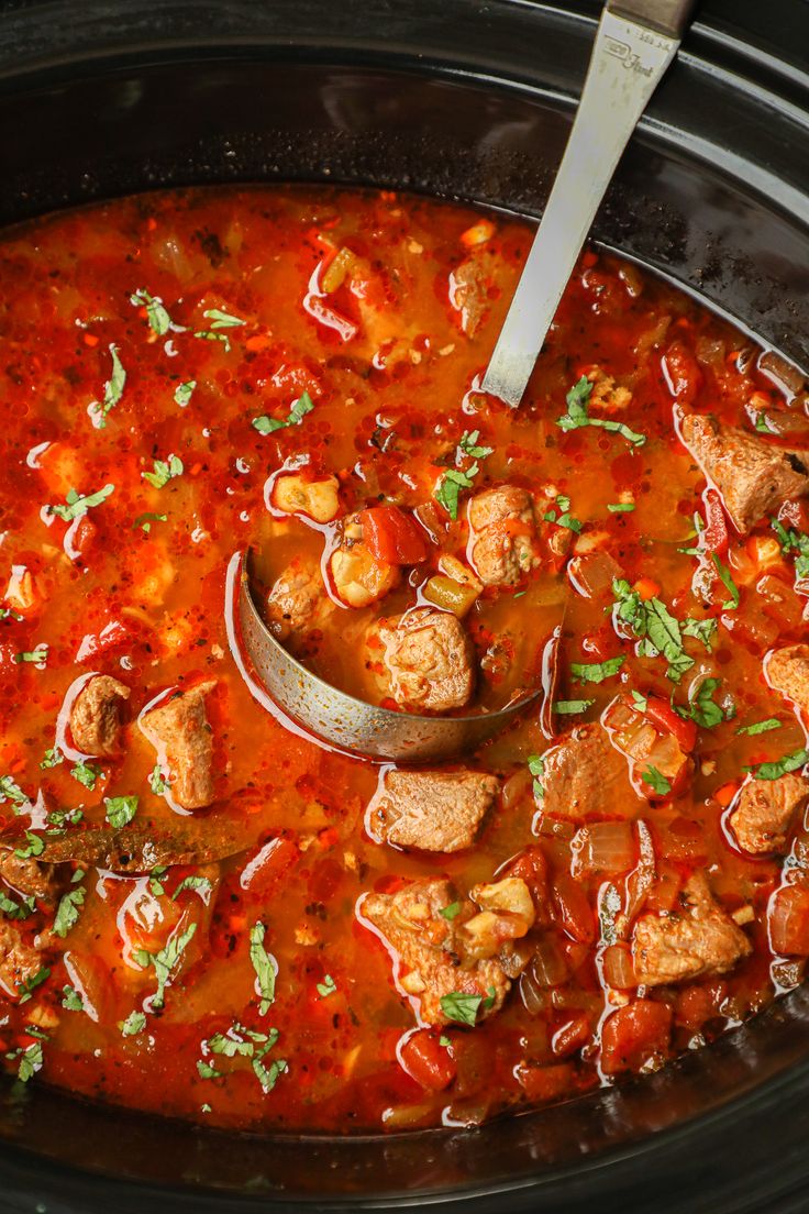 a wooden spoon in a slow cooker filled with meatballs and tomato sauce, garnished with parsley