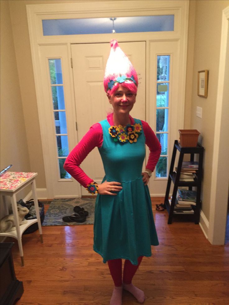 a woman in a green dress and pink hair wearing a party hat with flowers on her head