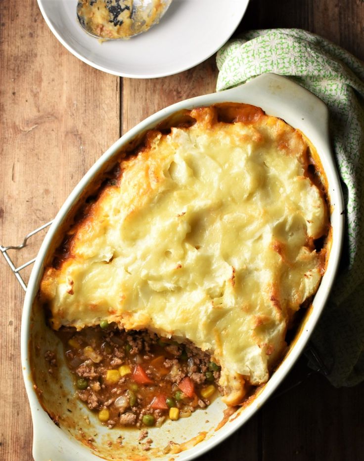 an oval casserole dish with meat and vegetables in it on a wooden table