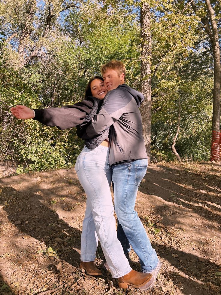 a man and woman are hugging in the woods