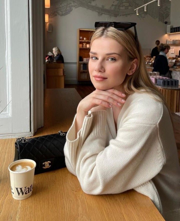 a woman sitting at a table with a coffee cup in front of her and looking off to the side